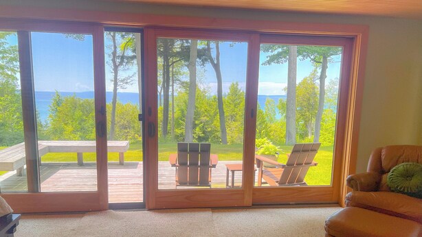 A room with a large sliding glass door leading to an outdoor deck with a table and chairs, and a leather chair inside.