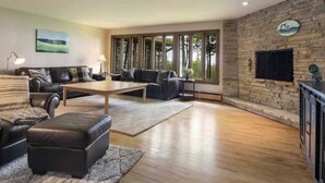 A spacious living room with a large window, a fireplace, and a flat-screen TV mounted on the wall.