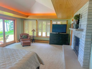 Un dormitorio con cama, una silla, un televisor sobre una cómoda y una chimenea.