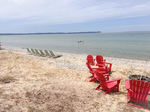 Una playa con sillas Adirondack rojas y verdes, una zona arenosa y una masa de agua tranquila.