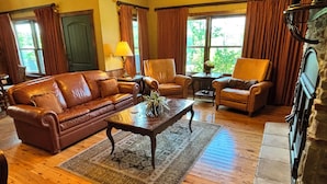 A cozy living room with a leather sofa, armchairs, a coffee table, and a fireplace. - Beautiful Cabin - Secluded But Convenient (Branson)