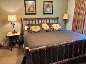 A bed with a dark wooden headboard, a small wooden nightstand with a lamp, and two framed leaf artworks on the wall.