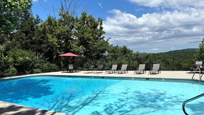 A clear blue swimming pool with lounge chairs and a red umbrella, surrounded by trees and a fence. - Beautiful Cabin - Secluded But Convenient (Branson)