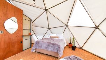 Una habitación tipo tienda con cama, un espejo redondo y dos plantas en macetas.