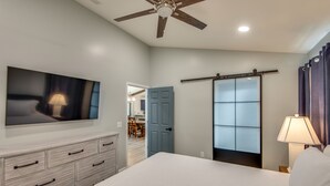 Ein Schlafzimmer mit einem Bett, einem an der Wand montierten Fernseher, einem Deckenventilator, einer Schiebetür und einem Nachttisch mit einer Lampe.