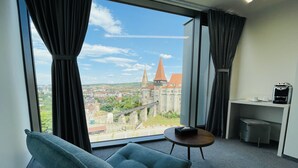 Une chambre d’hôtel dotée d’une grande fenêtre donnant sur un château historique et la ville environnante.