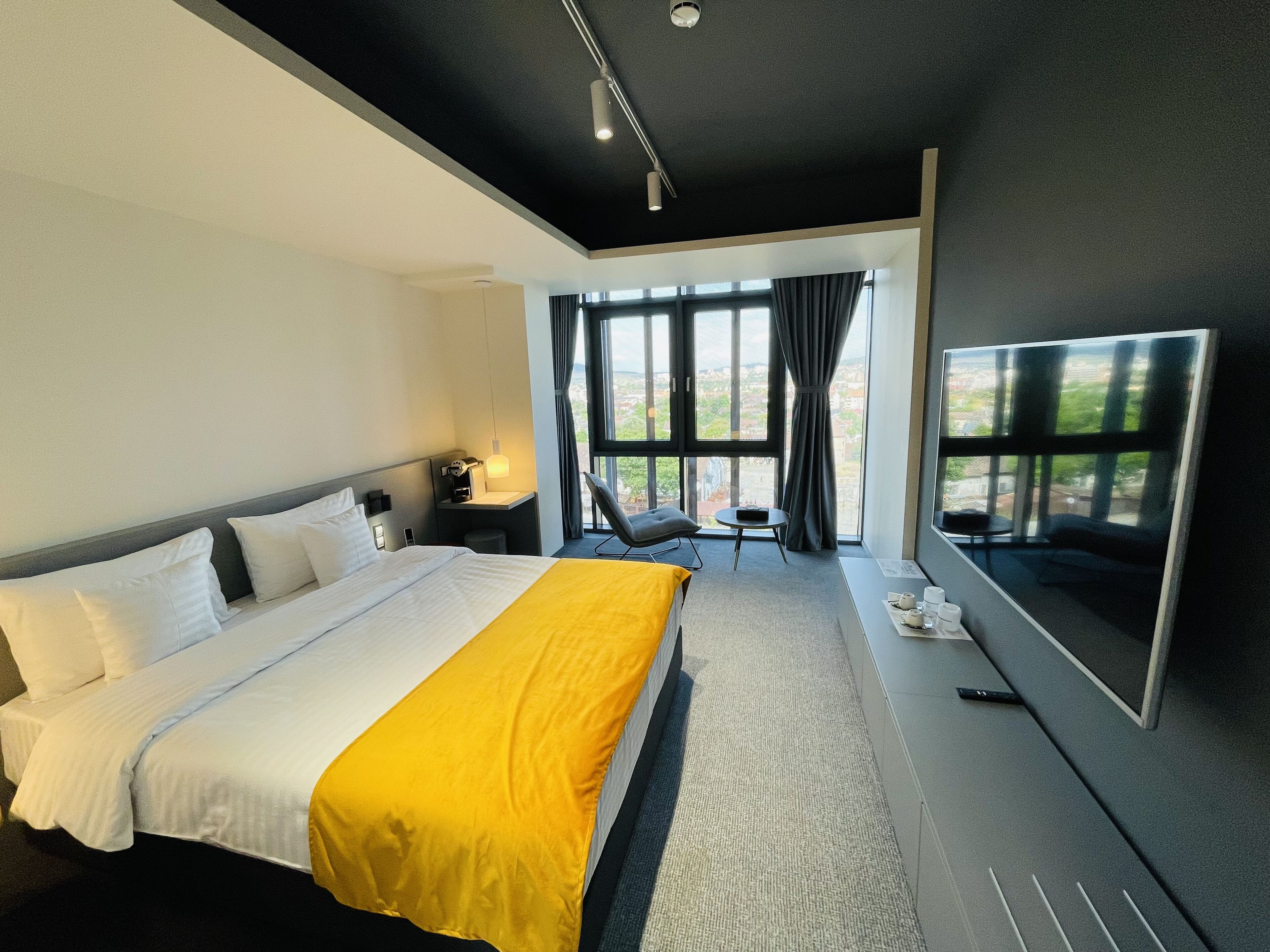 Een moderne hotelkamer met een groot bed, een bureau, een stoel en een groot raam met uitzicht op de stad.