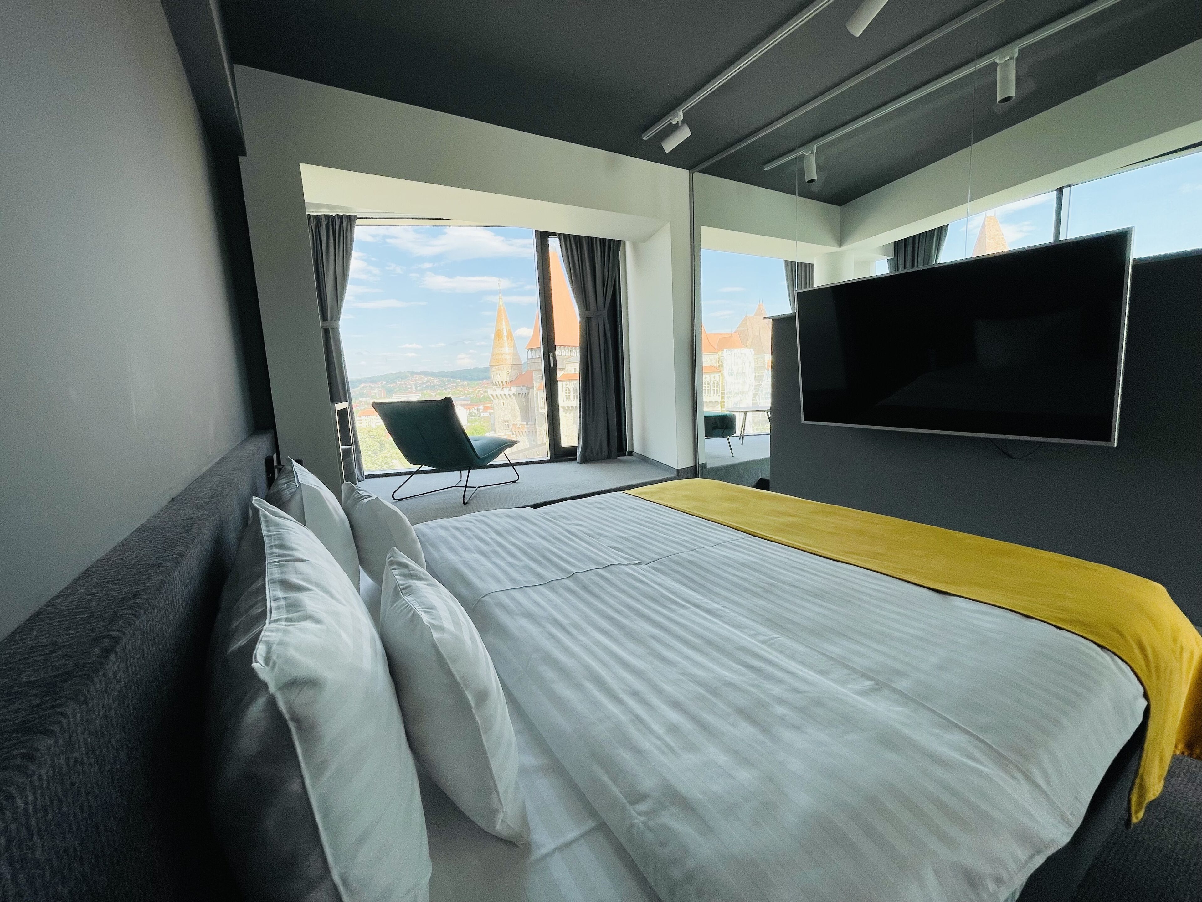A modern hotel room with a large bed, a flat-screen TV, and a view of a cityscape.