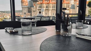 Une table à manger, agrémentée de sets de table, de couverts et de verres, se dressant sur fond d’un château aux toits rouges.