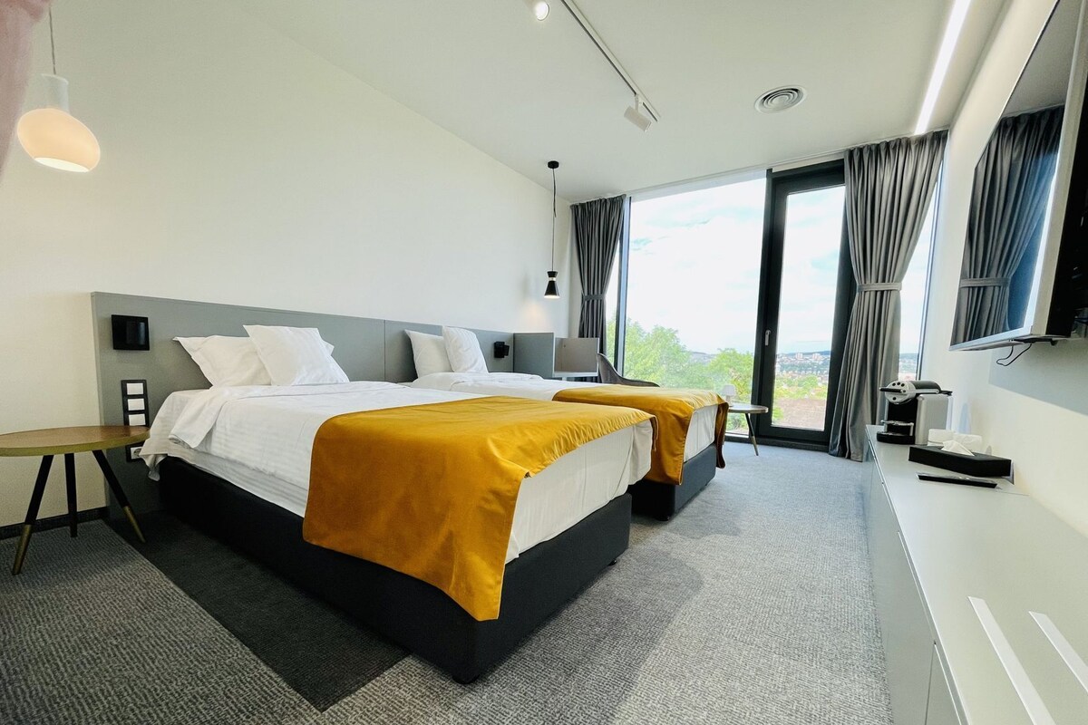Habitación de hotel moderna con una cama grande, un escritorio, una silla, un televisor y vistas al exterior.