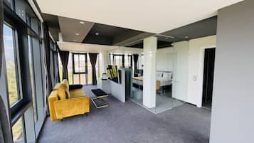 A modern hotel room with a large window, a yellow sofa, a small table, and a bed with a white headboard.
