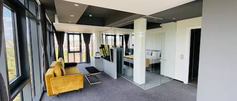 Ein modernes Hotelzimmer mit einem großen Fenster, einem gelben Sofa, einem kleinen Tisch und einem Bett mit weißem Kopfteil.
