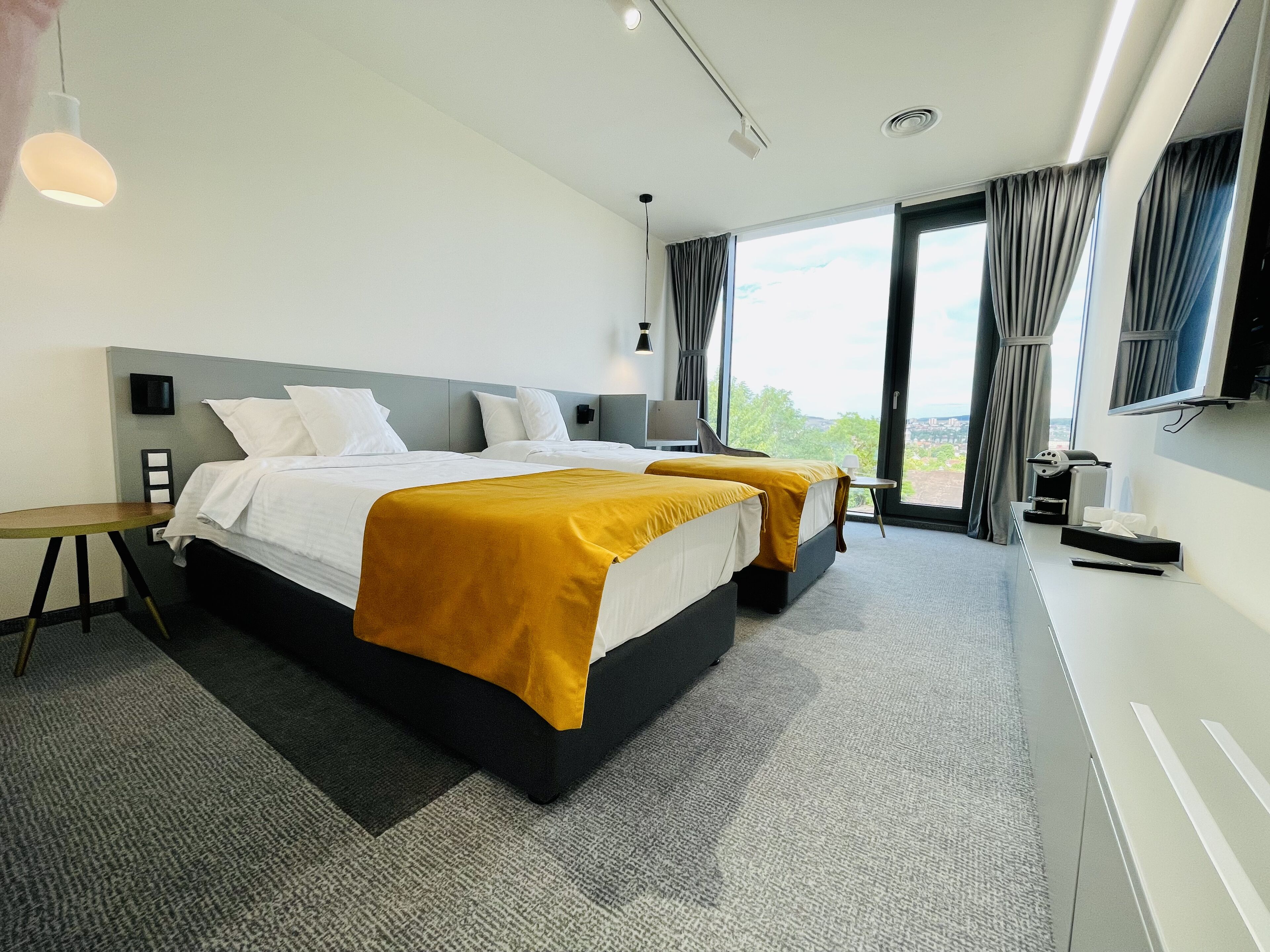 A modern hotel room with two beds, a desk, and a TV.