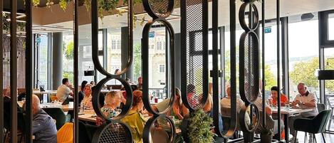 A modern restaurant with a unique geometric design, featuring circular and oval frames with plants, and a view of diners through large windows.