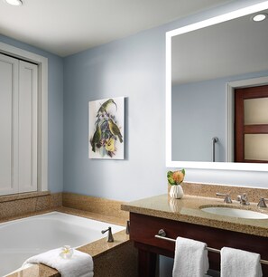 A modern bathroom with a bathtub, two sinks, a large mirror, and a framed artwork on the wall.