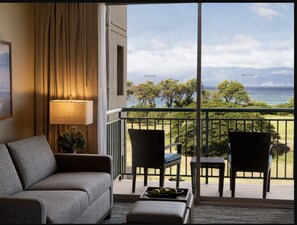 Relax on the balcony with ocean and mountain views, featuring a comfortable sofa and wicker chairs.