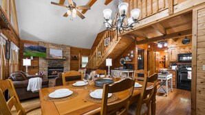 Un intérieur en bois comprenant une table à manger pour six personnes, une cheminée et un coin cuisine.