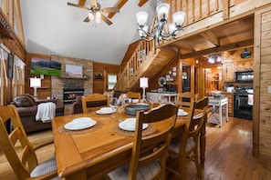 A wooden interior with a dining table set for six, a fireplace, and a kitchen area.
