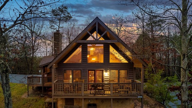 Une cabane dotée d’un balcon, d’une cheminée et offrant une vue sur la forêt environnante.