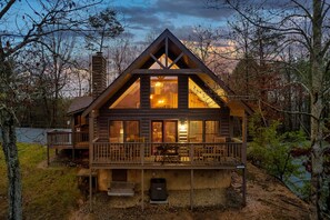 A cabin with a balcony, a fireplace, and a view of the surrounding forest.