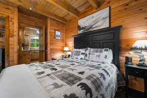 A wooden cabin bedroom with a bed, nightstand, lamp, and a painting on the wall.