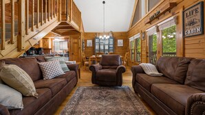 L’intérieur d’une cabane avec des murs en bois, un escalier, un coin repas et deux canapés en cuir.