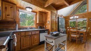 Une cuisine rustique aménagée dans une cabane en bois, avec un coin repas, des placards en bois, un évier et un lustre.