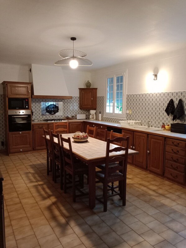 A kitchen with wooden cabinets, a dining table with chairs, a built-in oven, a microwave, and a hanging light fixture.
