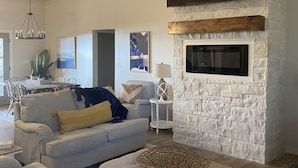 A living room with a stone fireplace, a flat-screen TV, a ceiling fan, and a dining area with a table and chairs. - “Lake Escape”- Lake House @ Lake of Arbuckle’s (Sulphur)