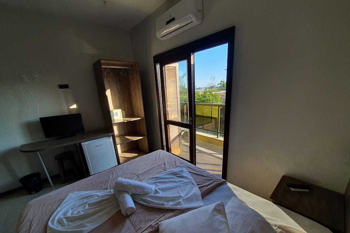 Une chambre d’hôtel équipée d’un lit, d’un bureau, d’une télévision, d’une armoire et d’un balcon avec vue.