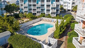 Une piscine entourée d’une clôture blanche, avec des immeubles à plusieurs étages en arrière-plan.