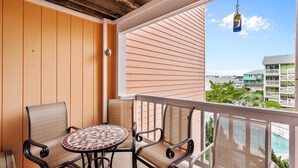 Un balcon avec une table ronde et quatre chaises, donnant sur une piscine et des immeubles.