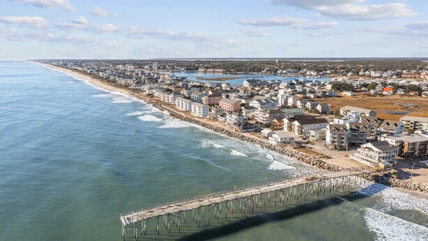 Une ville côtière dotée d’une jetée qui s’avance dans la mer, entourée d’immeubles résidentiels et bordée d’une plage.