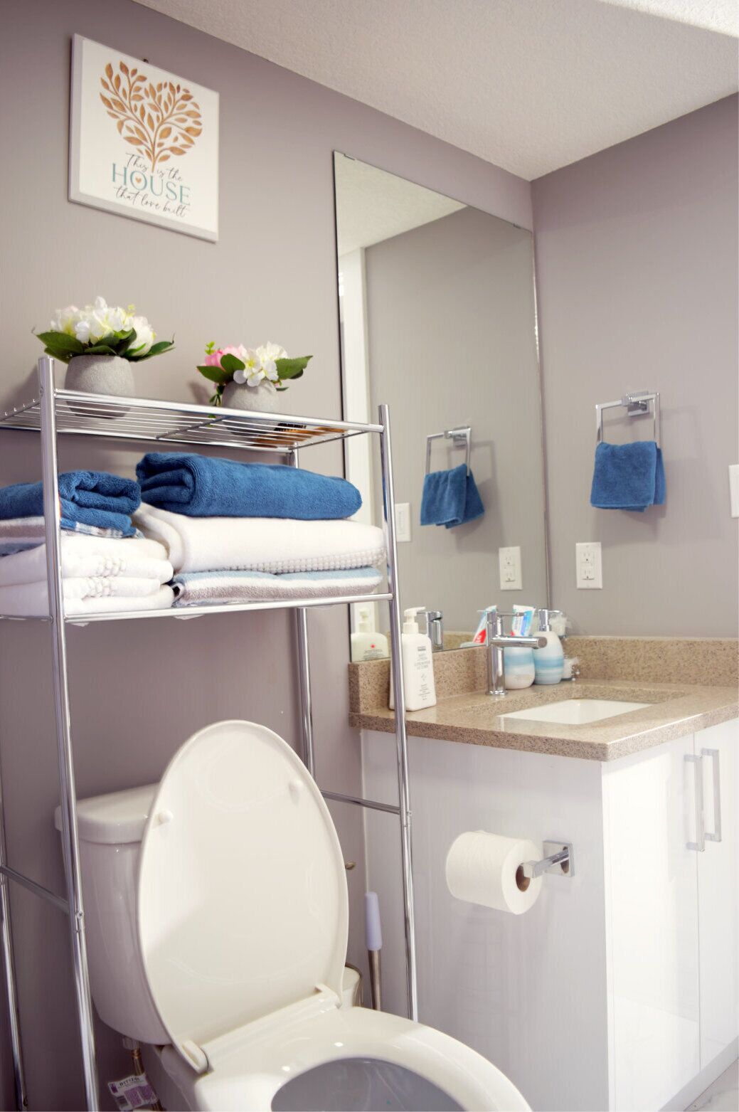 Un baño moderno con un inodoro blanco, un lavamanos con encimera de granito y un perchero con toallas azules.