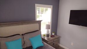 A bedroom with a bed, a nightstand, a lamp, a clock, and a TV mounted on the wall.