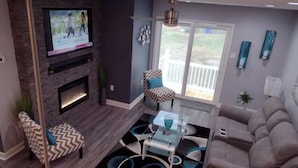 A modern living room with a fireplace, a television mounted on the wall, a sofa, a coffee table, and a patterned rug.