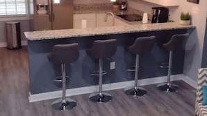 A modern kitchen with a central island, bar stools, stainless steel appliances, and pendant lighting.