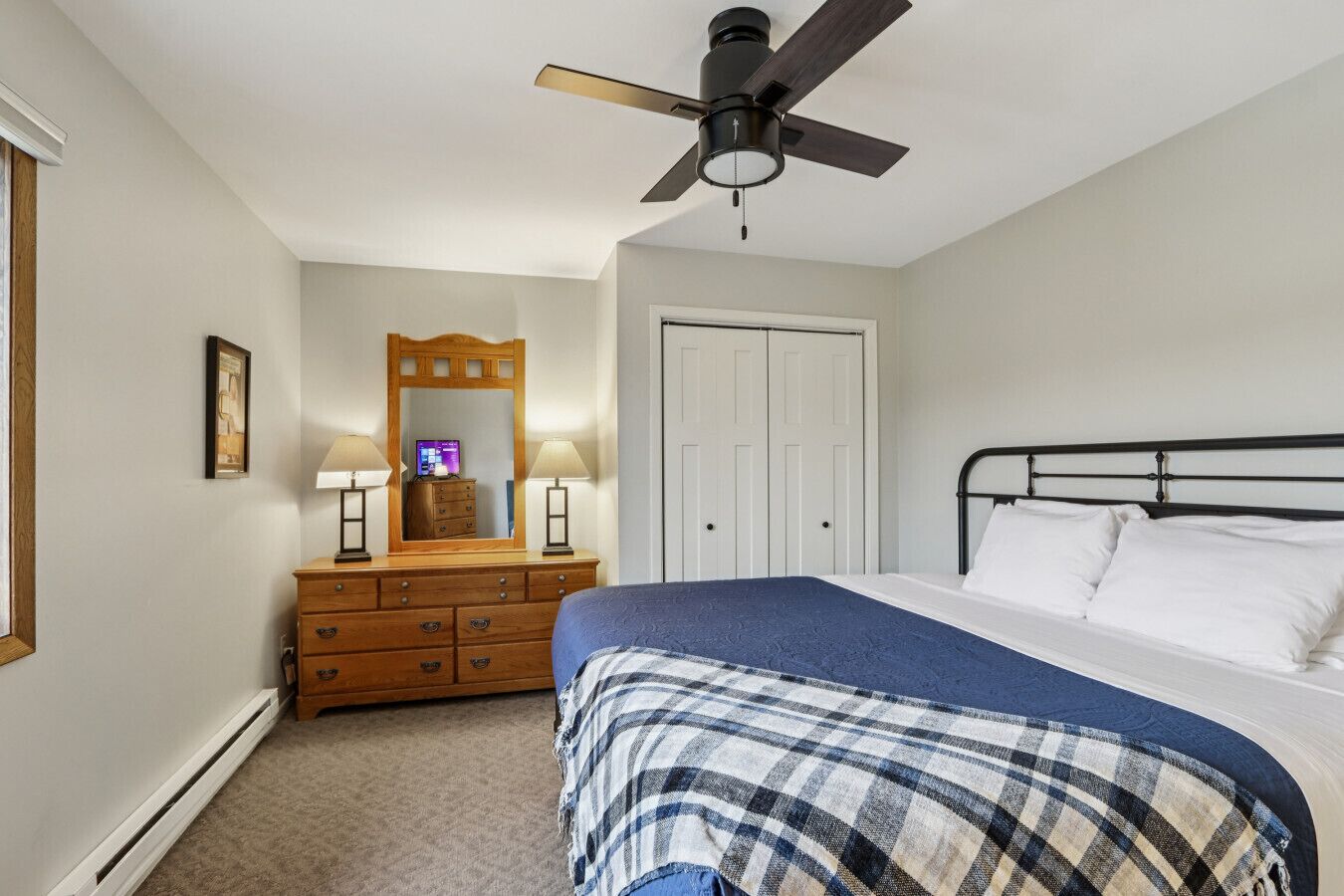 Quarto com cama, cômoda, espelho, ventilador de teto e porta.