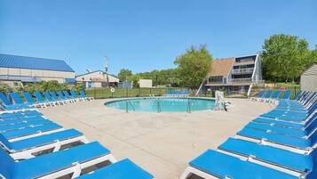 A pool area with blue lounge chairs arranged around it, a clear sky, and buildings in the background.