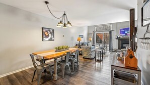 Ein modernes Wohnzimmer mit Kamin, einem Essbereich mit Holztisch und -stühlen sowie einer Küchenzeile mit Bar.
