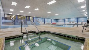 Ein großes Hallenbad mit mehreren Bahnen, einem Sprungbecken und einem Zuschauerbereich mit Tribünen.