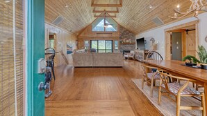 A spacious living area with a high ceiling, wooden beams, a large wooden dining table, and a cozy fireplace. - Lake Lure Family Escape | Sleeps 10 | Bunk Room | Hot Tub | Near Chimney Rock (Lake Lure)