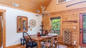 A wooden interior with a dining table set for four, surrounded by chairs. A chandelier hangs from the ceiling, and a mirror is mounted on the wall. - Lake Lure Family Escape | Sleeps 10 | Bunk Room | Hot Tub | Near Chimney Rock (Lake Lure)