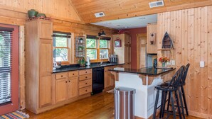 A wooden interior with a kitchen area featuring wooden cabinets, a black countertop, and a small bar with stools. - Lake Lure Family Escape | Sleeps 10 | Bunk Room | Hot Tub | Near Chimney Rock (Lake Lure)