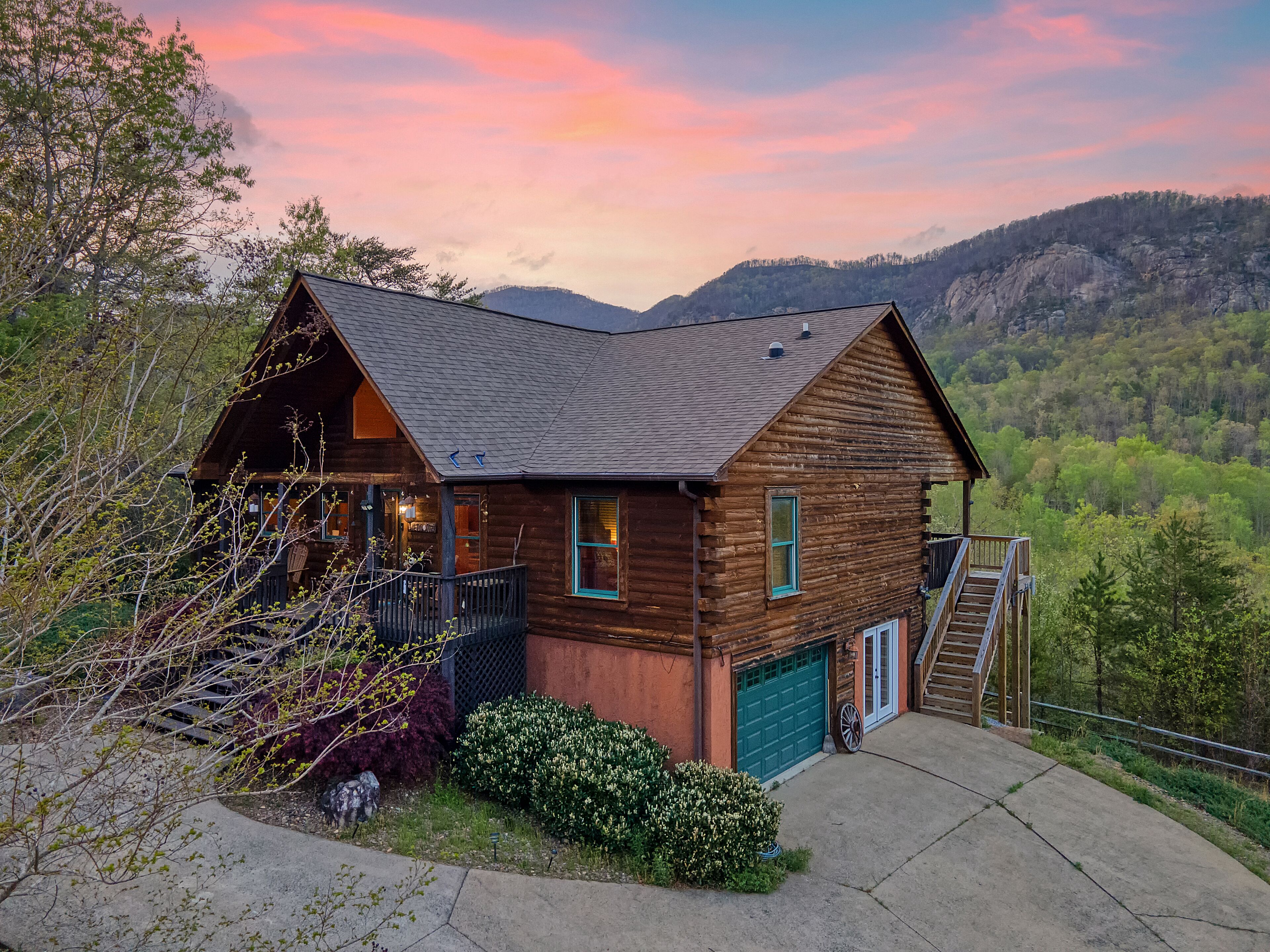 A log cabin with a garage, a porch, and a staircase leading to a deck.