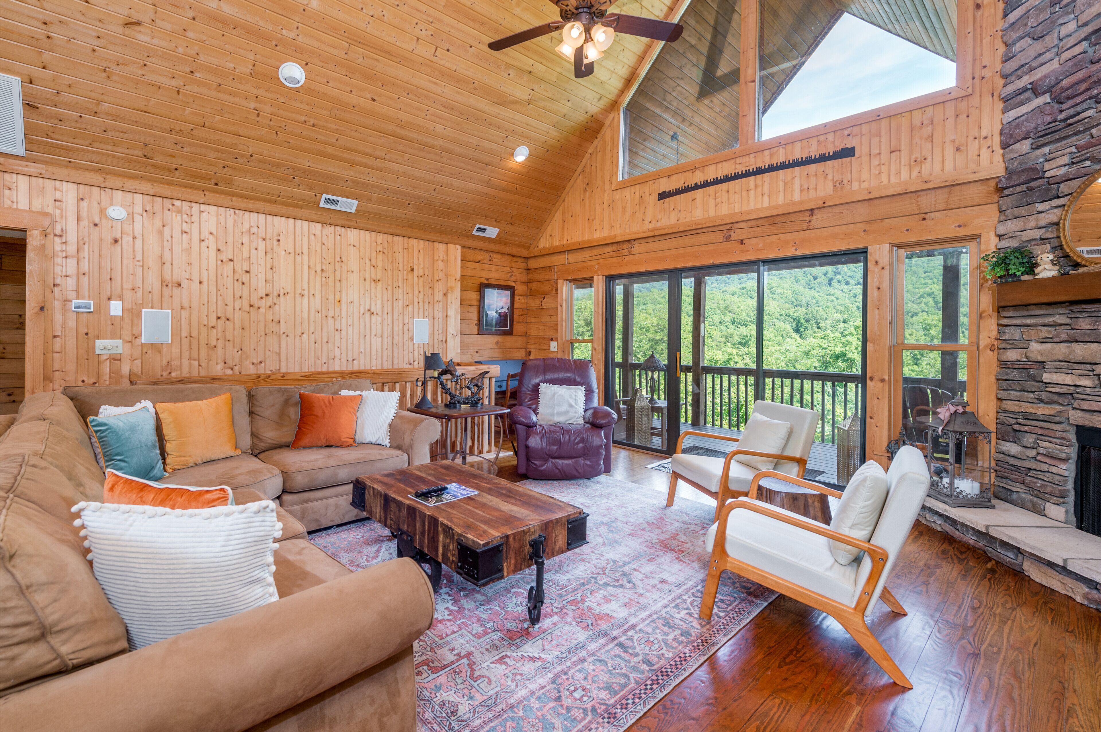 A spacious living room with a wooden ceiling, large windows, a stone fireplace, and a cozy seating area.