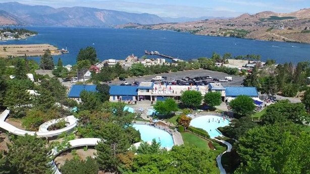 A resort with multiple swimming pools, a large building with a blue roof, and a view of a lake and mountains.