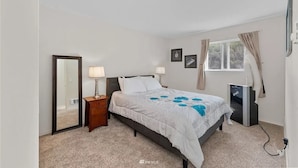 A bedroom with a bed, bedside lamps, a mirror, a window with curtains, and a TV.