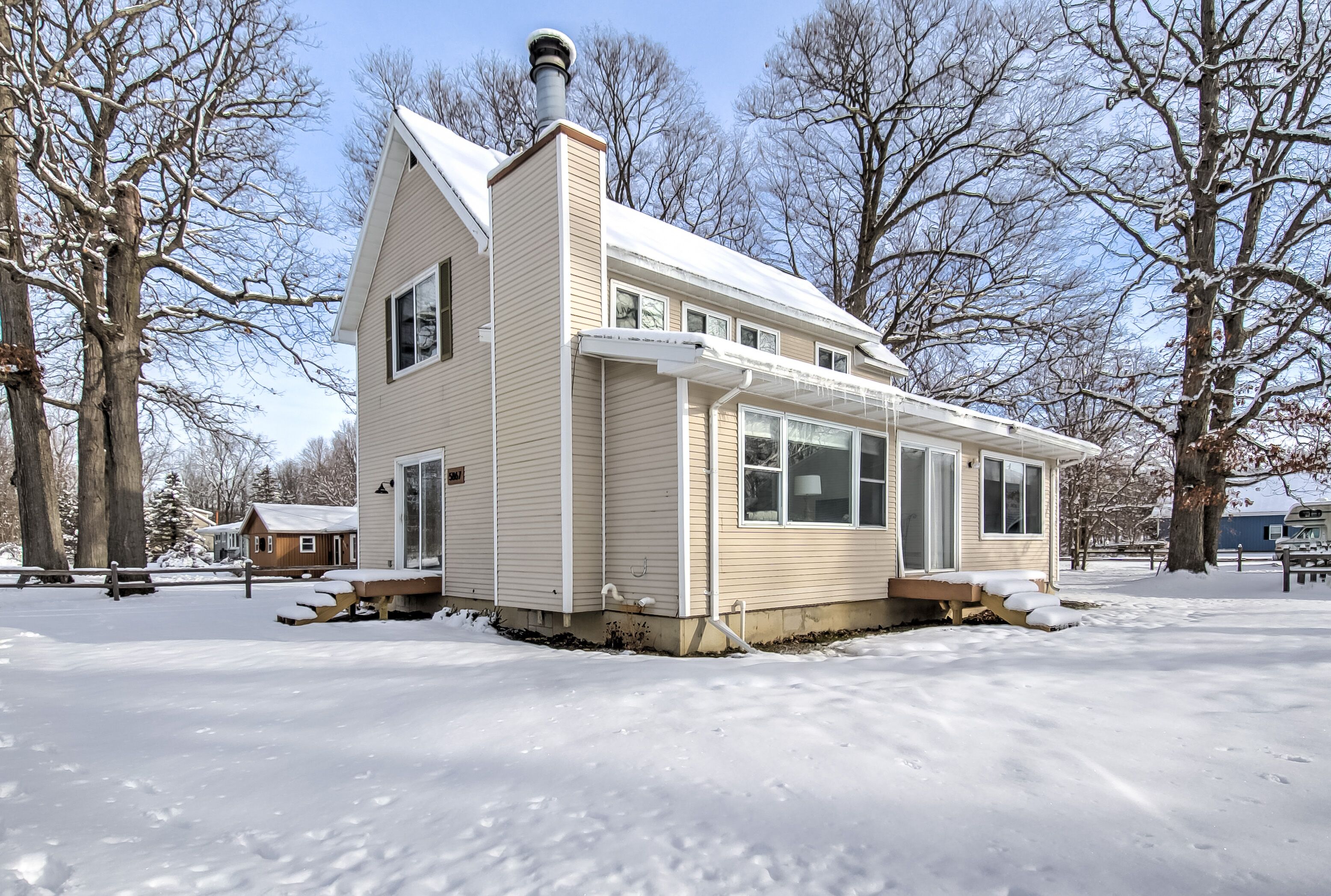 A single-story house with a gabled roof and a chimney, surrounded by snow-covered ground and leafless trees.