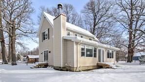 A single-story house with a gabled roof and a chimney, surrounded by snow-covered ground and leafless trees.